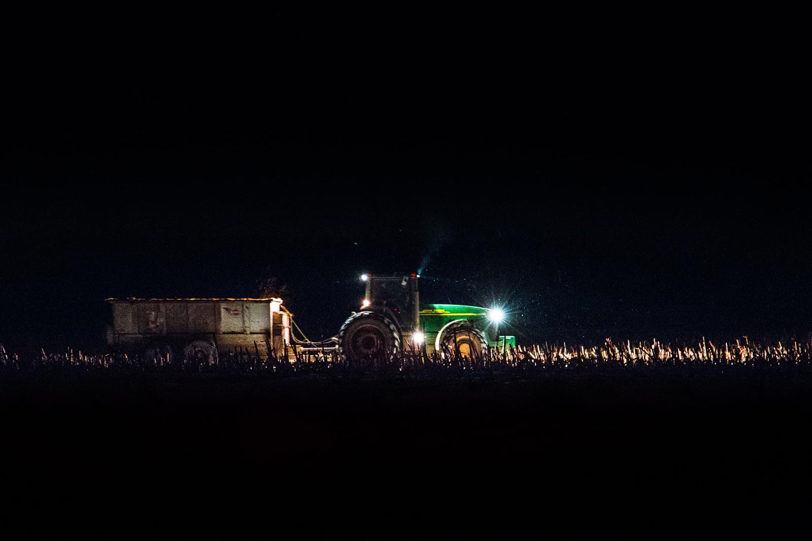 Traktor på åker skördar på natten